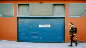 A man walks past a blue garage on an urban street, capturing the vibrant city life.