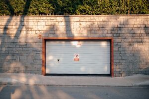 A garage entrance set in a brick wall with no parking signs. Sunlit with tree shadows.